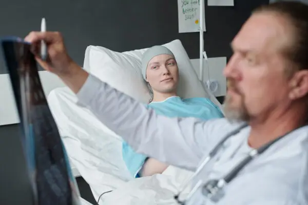 Young woman with brain cancer lying in bed and looking at doctor