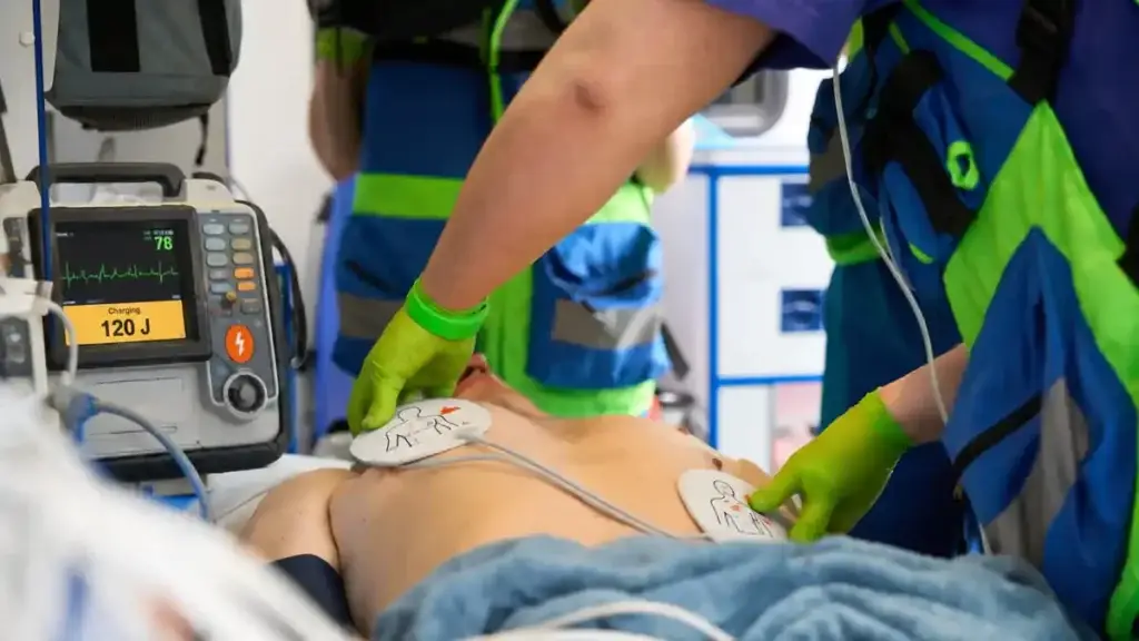 Clinicians applying defibrillator pads during resuscitation, with the defibrillator charging to 120 J